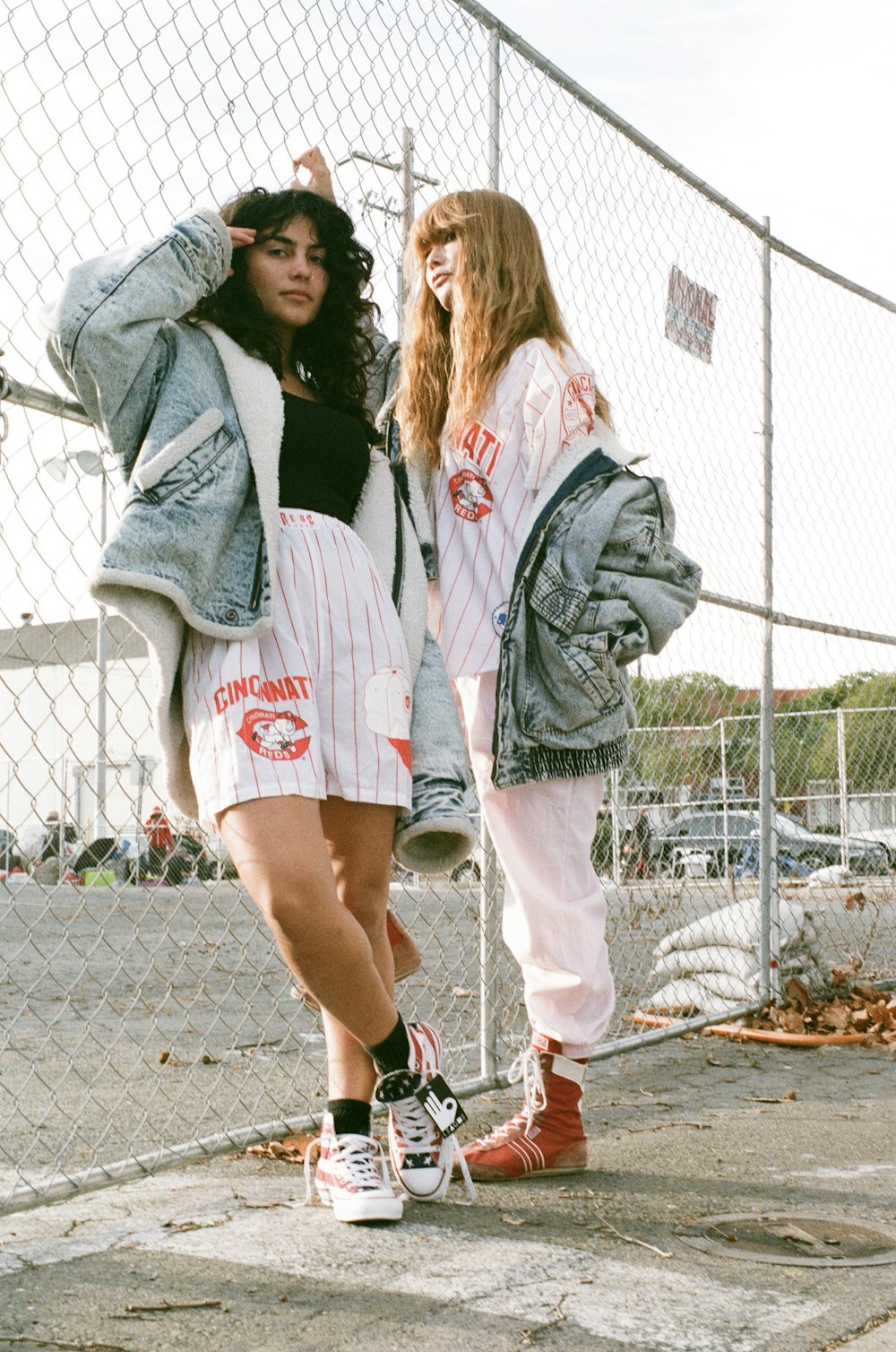 two women standing next to each other near a fence