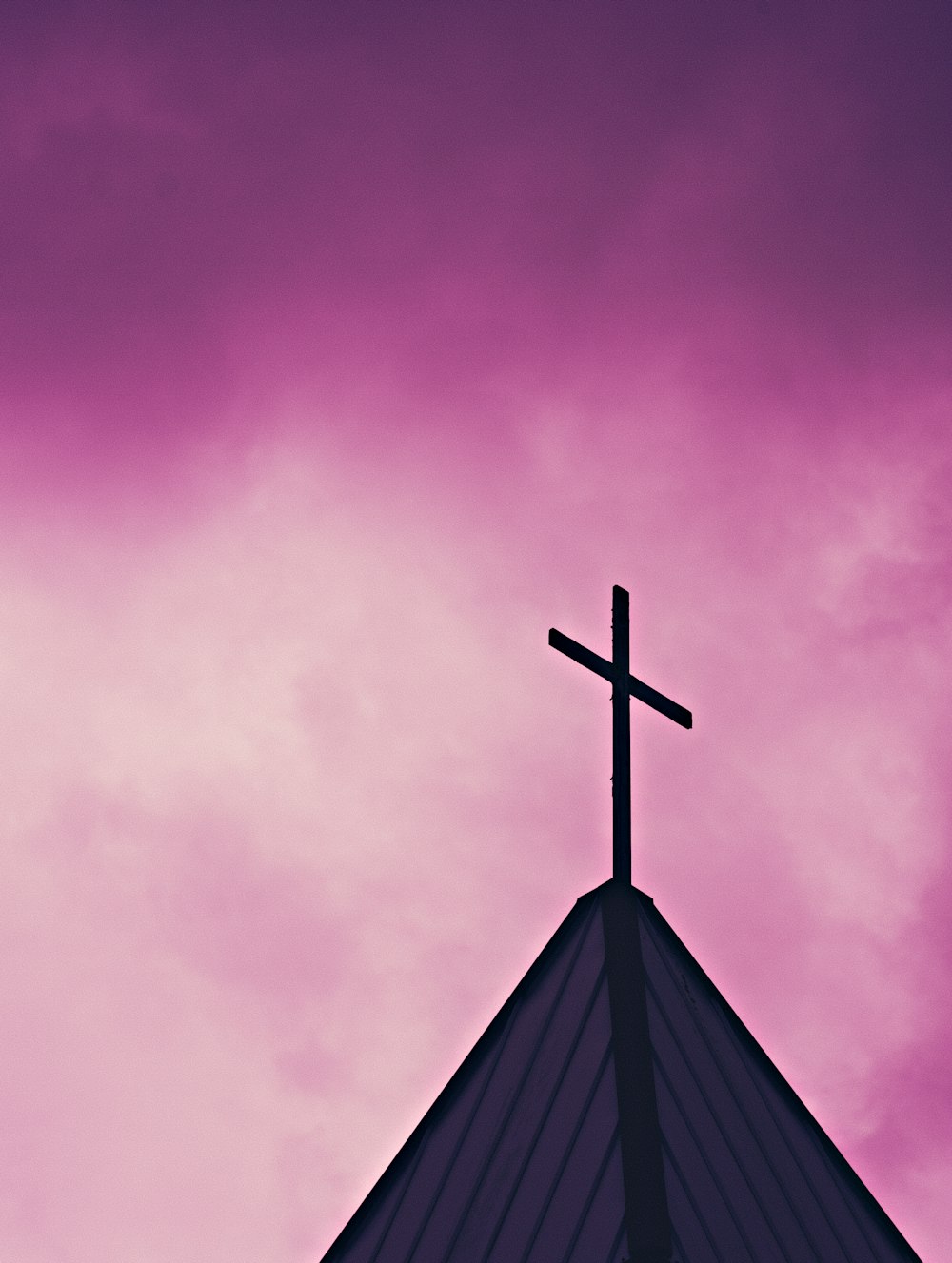 a cross on top of a church steeple against a purple sky