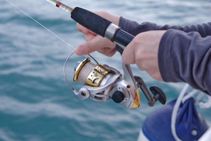 Bare hands holding a spinning rod and reel over choppy blue sea, a gray long sleeve covering the forearm