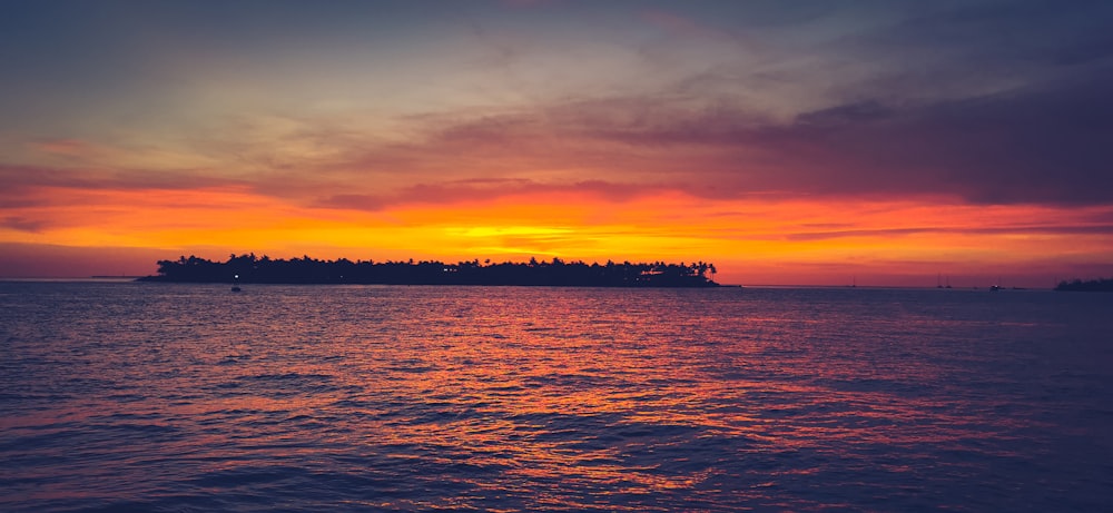 a sunset over a body of water with a small island in the distance