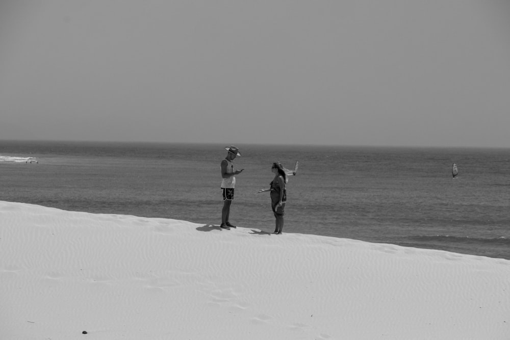 a couple of people standing on top of a sandy beach