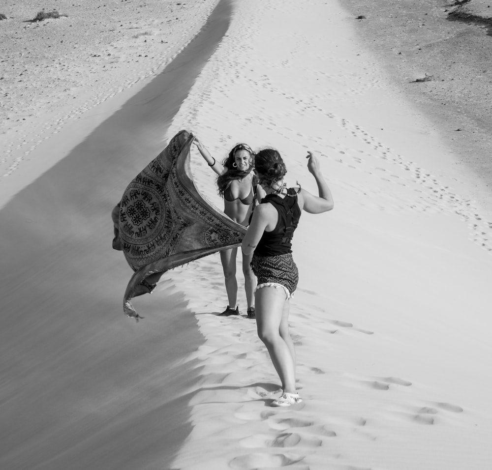 two women are walking in the sand with a scarf