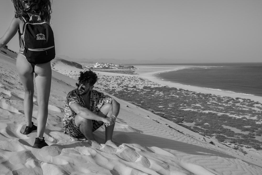 a man sitting on top of a sandy beach next to a woman