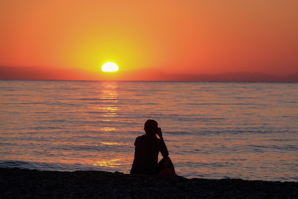 a person sitting on a beach at sunset