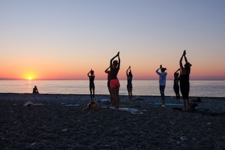 a group of people standing on top of a beach giving praise doing yoga