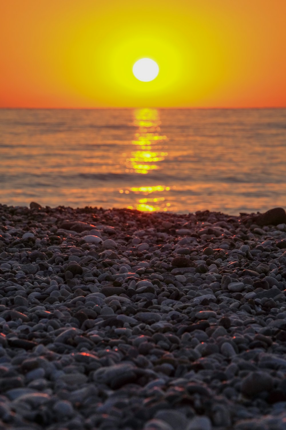 the sun is setting over the ocean on a rocky beach