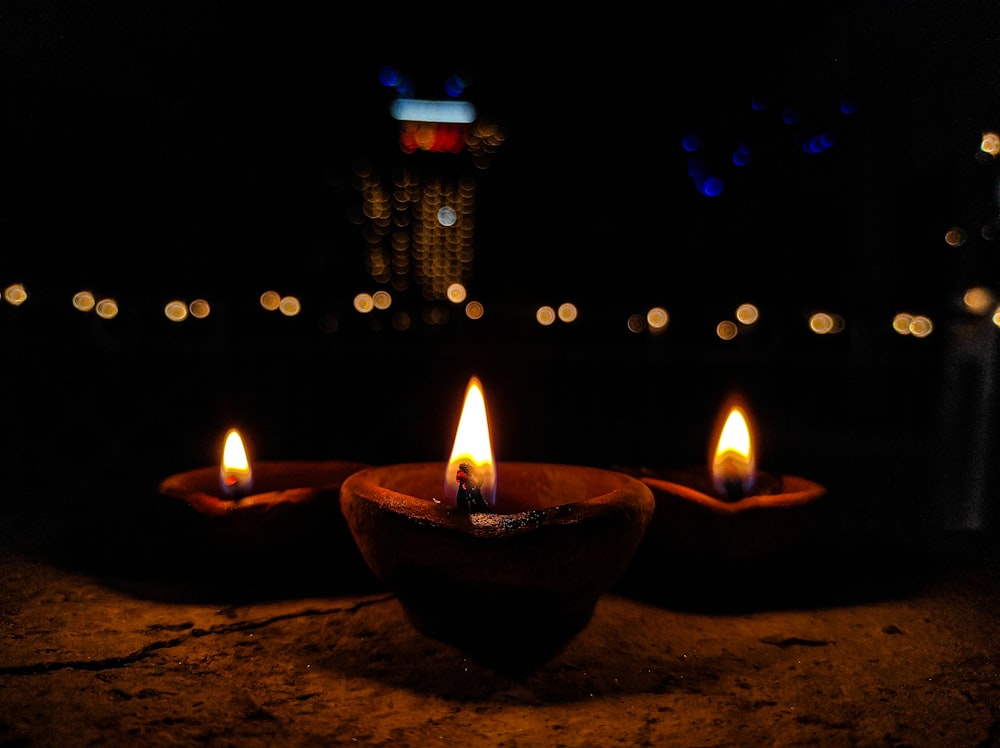 três velas acesas sentadas em uma tigela em uma mesa