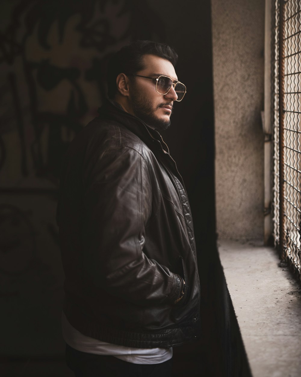 a man in a leather jacket and sunglasses leaning against a window