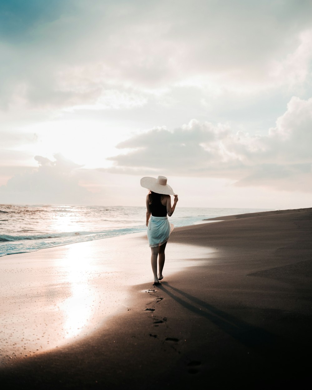 a woman in a white hat walks along the beach