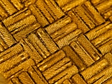 A close-up view of intricately arranged gold-colored metal pieces with a textured, crisscross pattern. The light reflects off the metallic surface, enhancing the luxurious appearance.