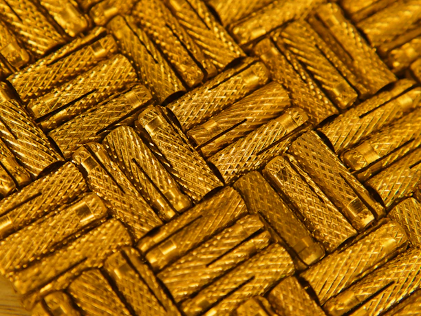 A close-up of textured gold metal with sharp geometric cuts reflecting light.