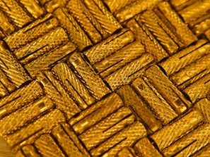 A close-up view of intricately arranged gold-colored metal pieces with a textured, crisscross pattern. The light reflects off the metallic surface, enhancing the luxurious appearance.