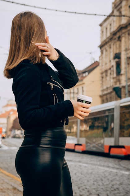 Woman in a dark jacket holding a takeaway coffee cup on a city street