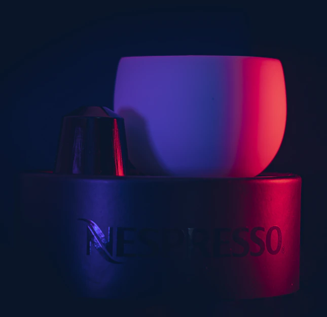 Close-up of a steaming cup of coffee next to a box of Nespresso capsules branded with Rosemoka colors