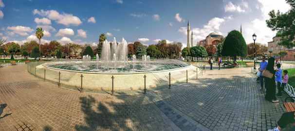 A panoramic view of Skanderbeg Square bustling with locals and tourists amidst elegant fountains and historic buildings.