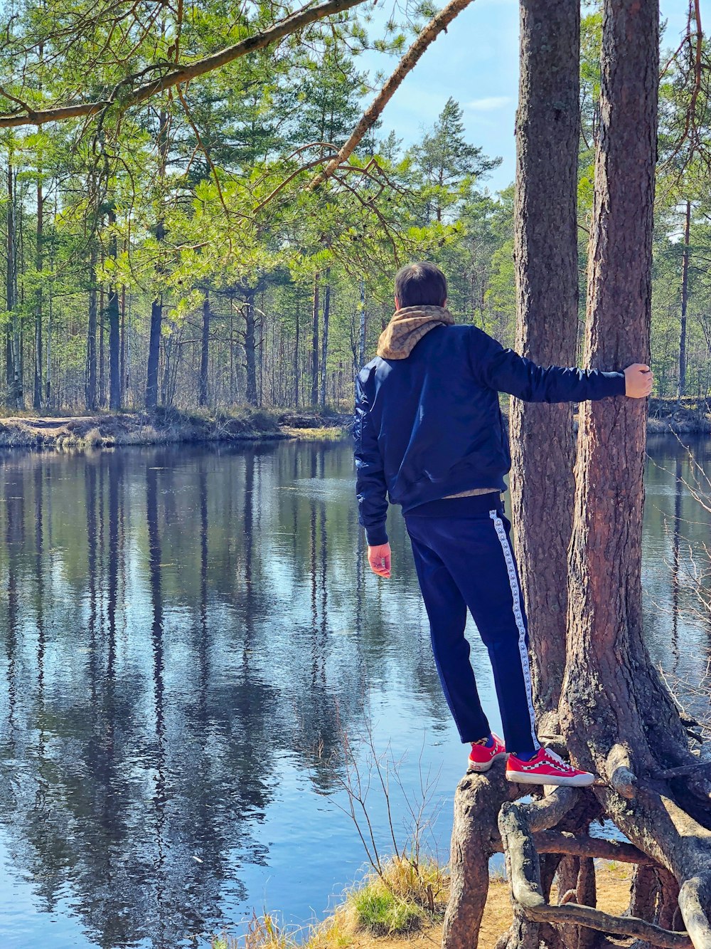 a man standing on a tree trunk next to a lake