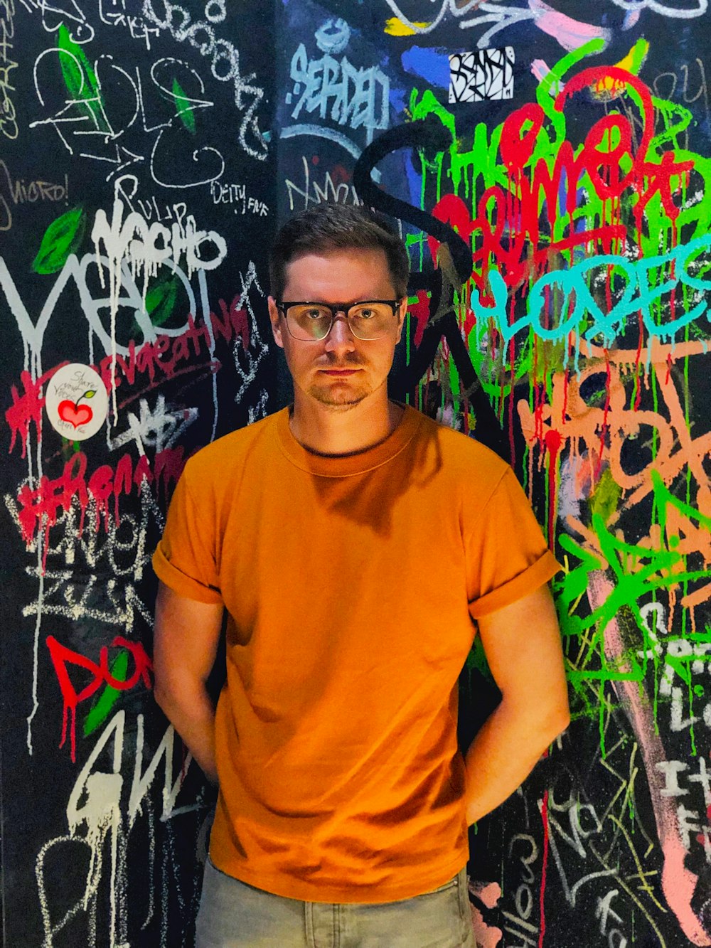 a man standing in front of a wall covered in graffiti