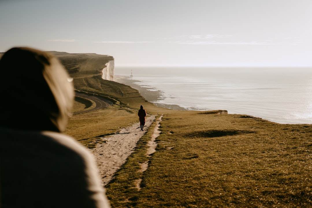 a person walking down a path next to the ocean, Seven Sisters Cliffs