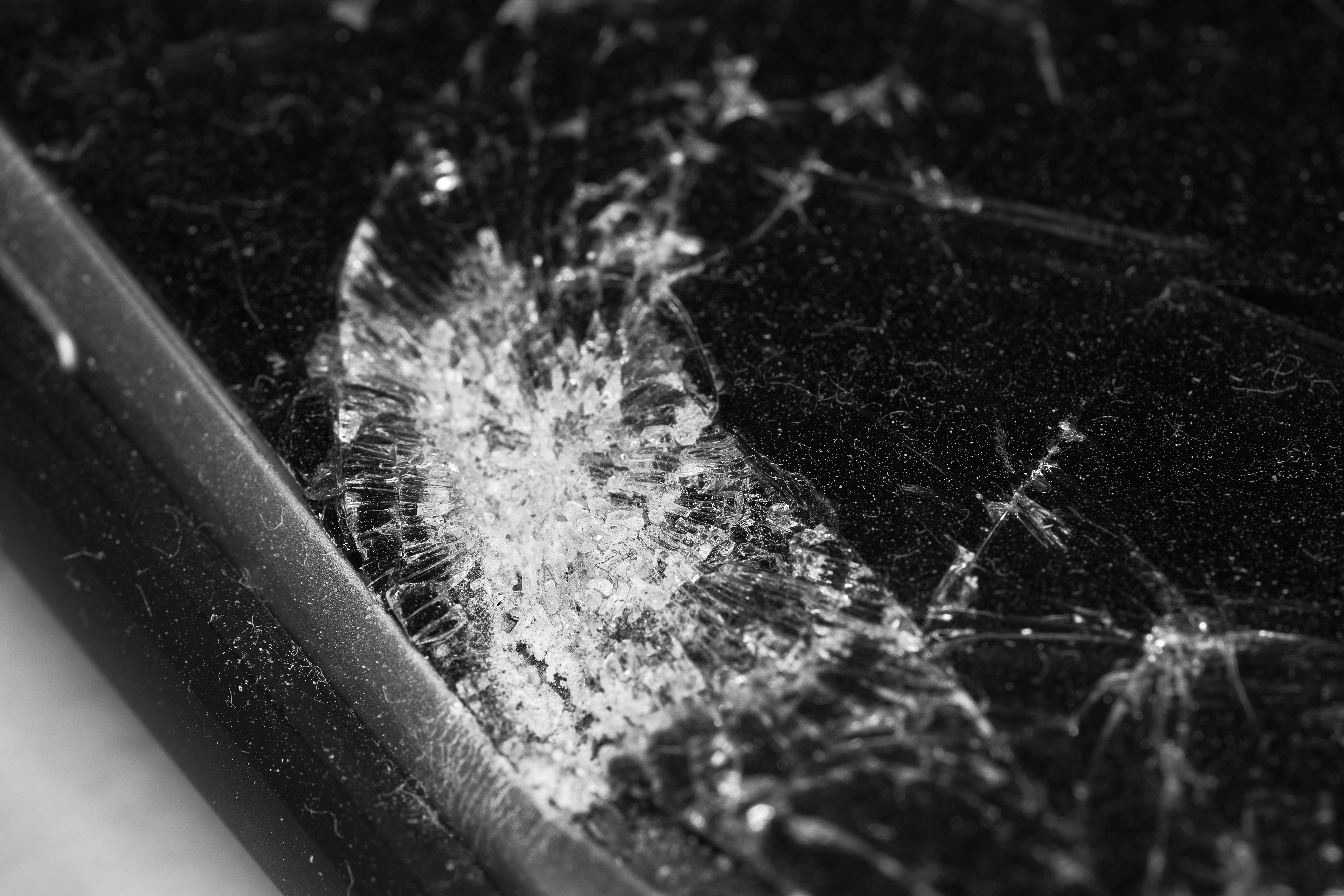 Cracked phone screen close-up, dark background, shattered glass visible