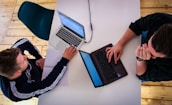 two men sitting at a table working on laptops