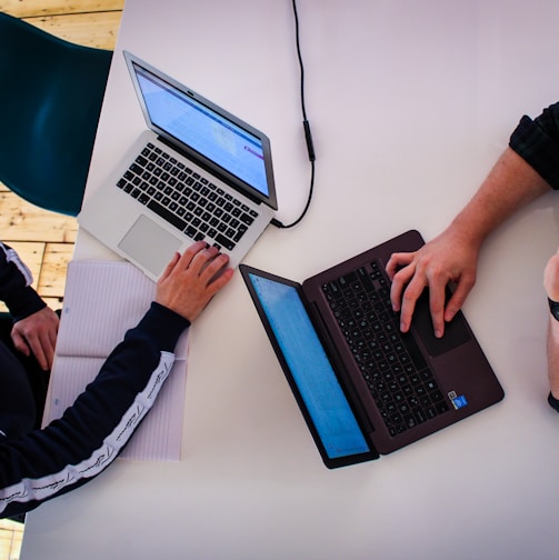 two men sitting at a table working on laptops