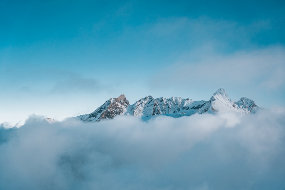 a mountain covered in snow and clouds under a blue sky