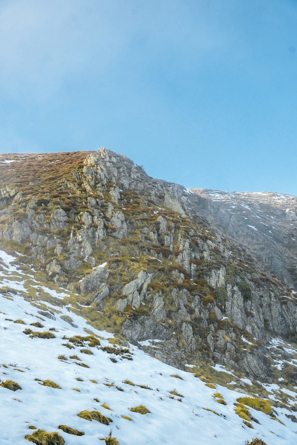 a mountain covered in snow and grass under a blue sky