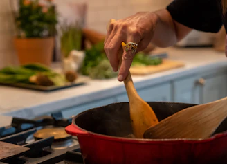 Close-up of a hand stirring a colorful vegetable stew in a cast iron skillet.