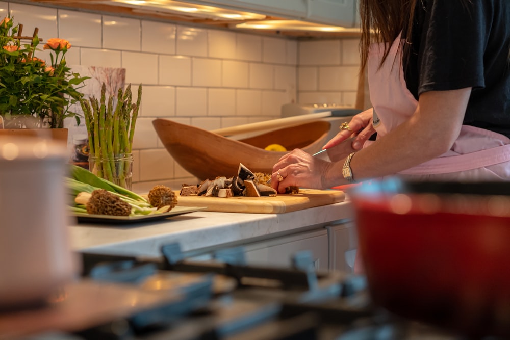 Una mujer en una cocina cortando verduras en una tabla de cortar