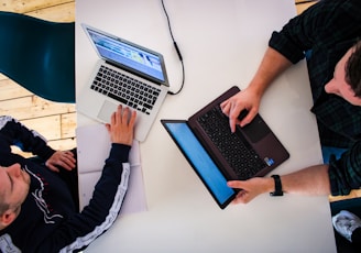 two men sitting at a table working on laptops