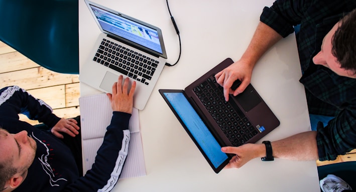 two men sitting at a table working on laptops