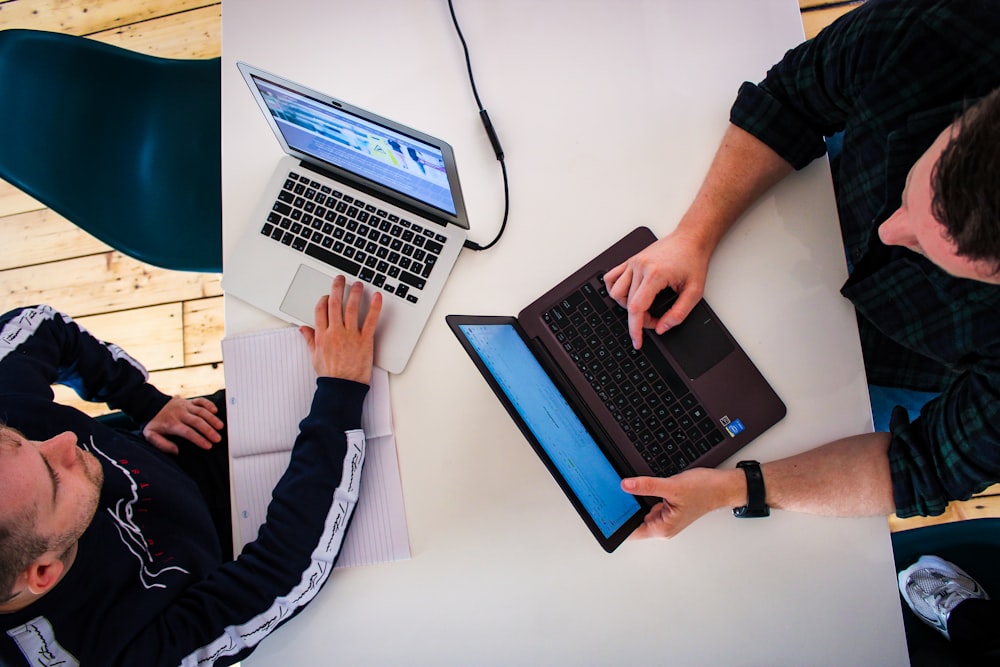 two men sitting at a table working on laptops