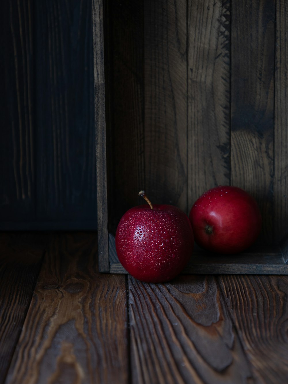 two red apples sitting in a wooden crate
