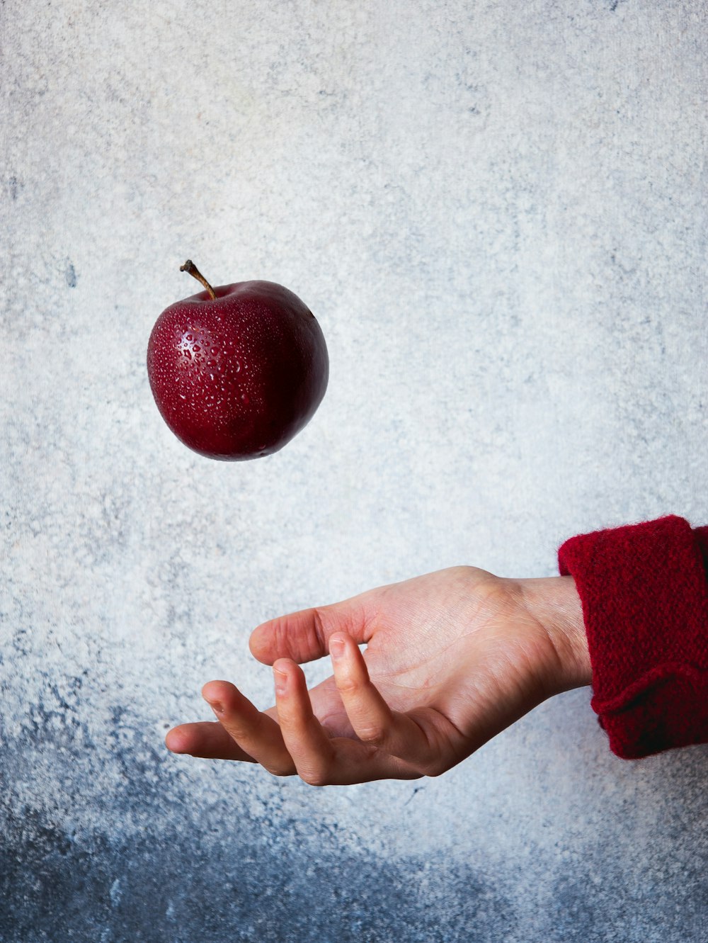 a hand reaching for an apple that is falling into the air
