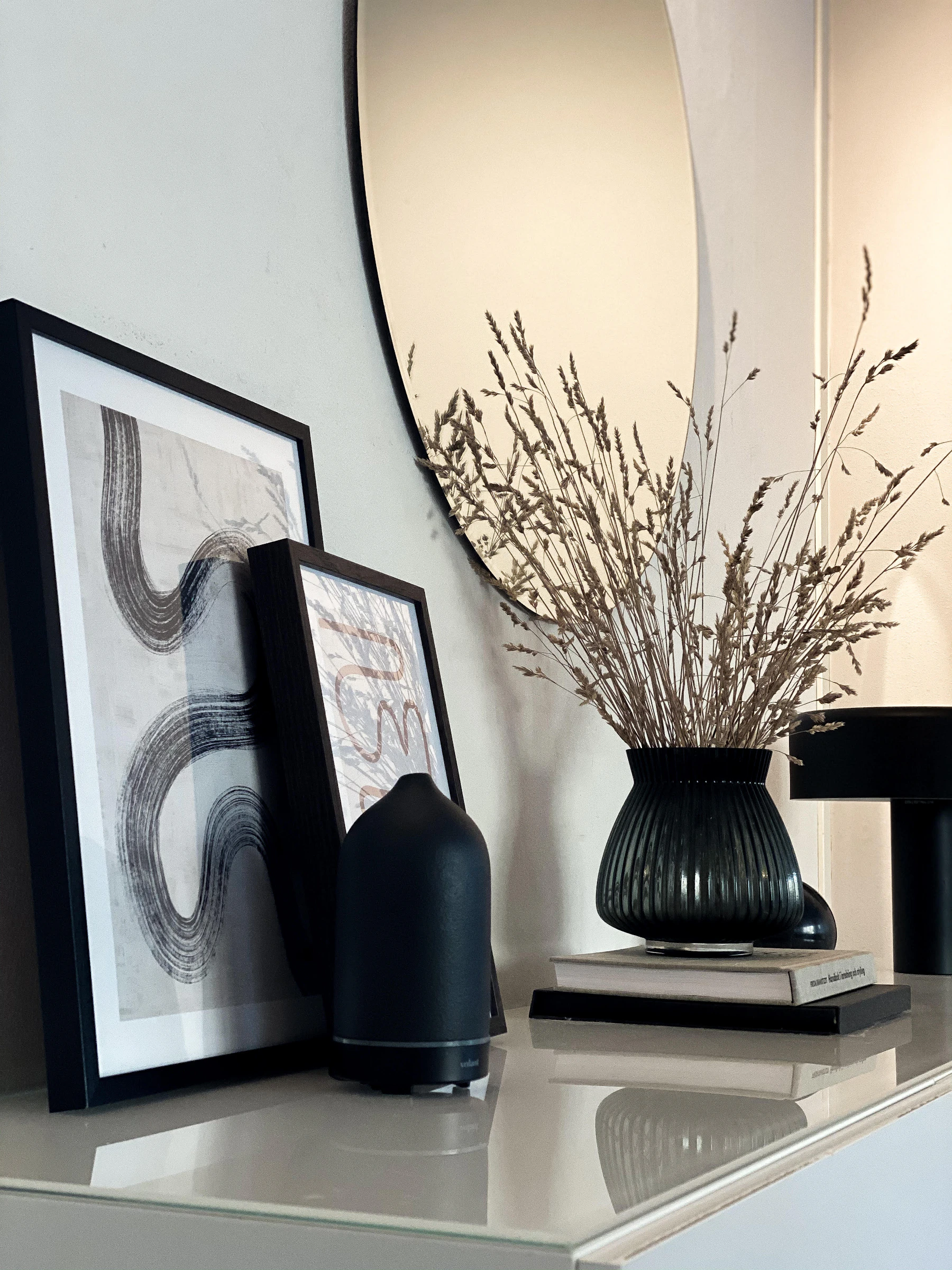 Elegant oval mirror styled with sculptural black ceramics, framed art and natural dried branches