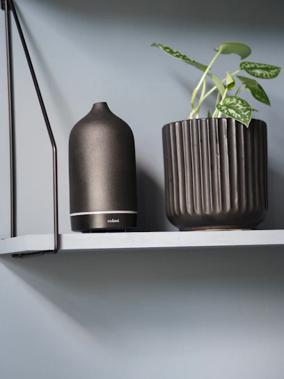 Modern room diffuser placed on a minimalist wooden shelf with soft ambient lighting.
