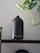 A collection of essential oil diffusers placed on a wooden shelf surrounded by green plants.