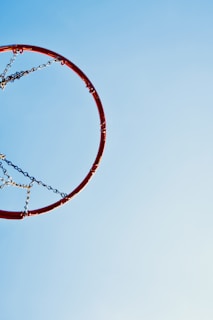 Close-up of a vibrant red basketball net swaying gently on an outdoor court under a clear blue sky.