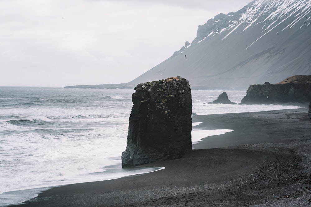 a large rock sticking out of the ocean next to a beach