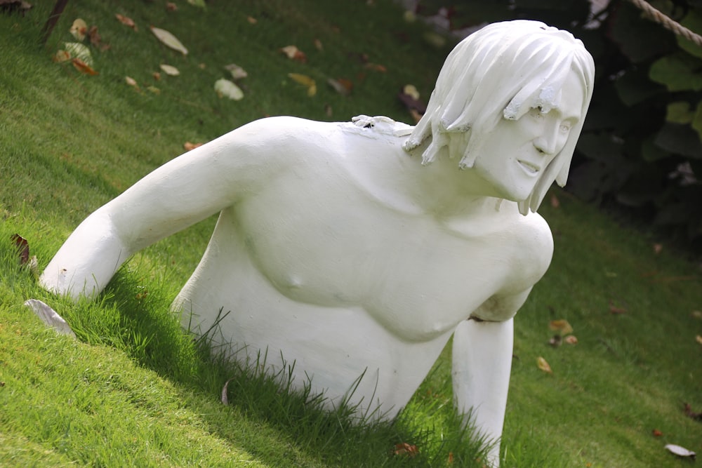 a white statue of a man sitting in the grass