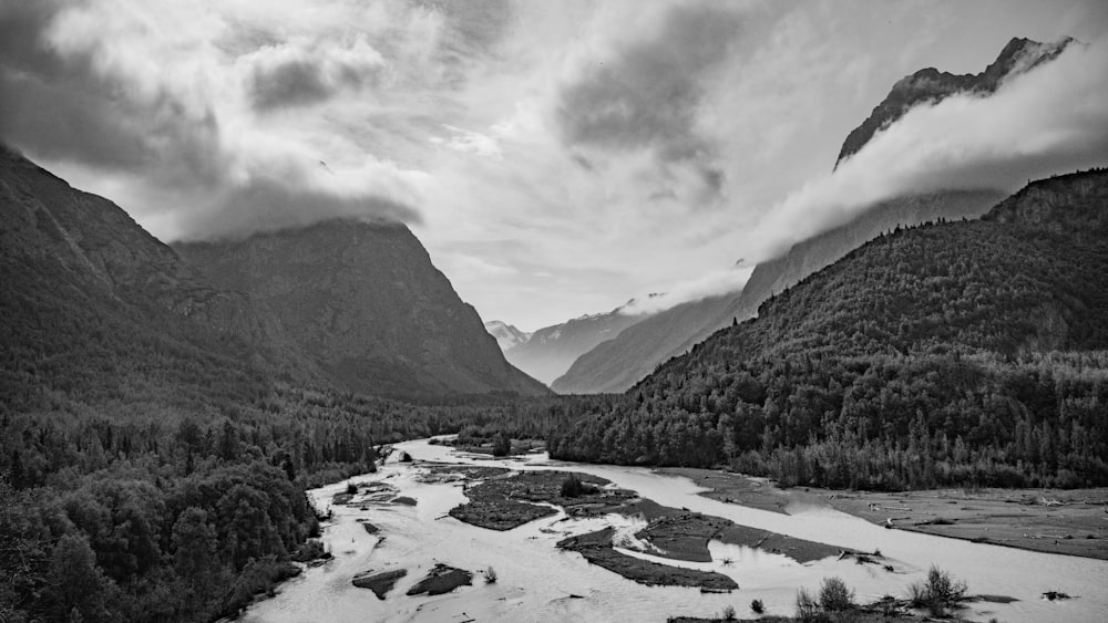 a black and white photo of a river and mountains