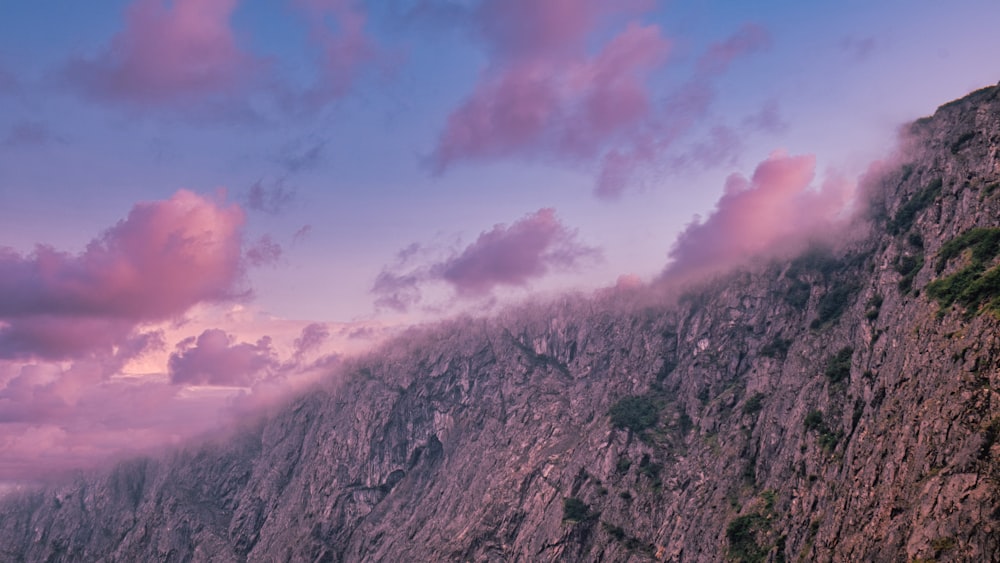 a mountain side with a cliff and clouds in the sky