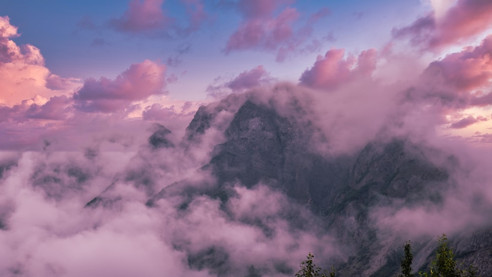 a mountain covered in clouds and trees under a cloudy sky