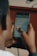 A person is holding a smartphone with both hands, reading a chat conversation on the screen. The chat messages are visible, containing text and emojis. The background is blurred and has a warm tone, indicating a possibly indoor environment.