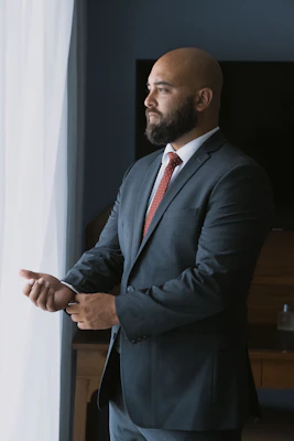 a bald man in a suit standing next to a window