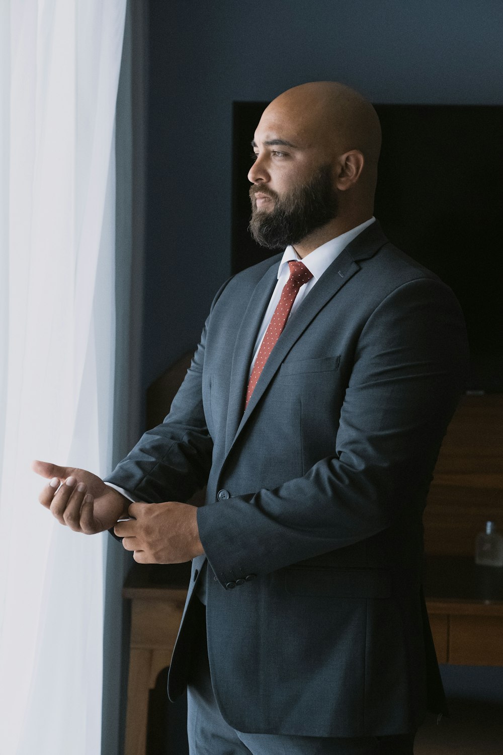 a bald man in a suit standing next to a window