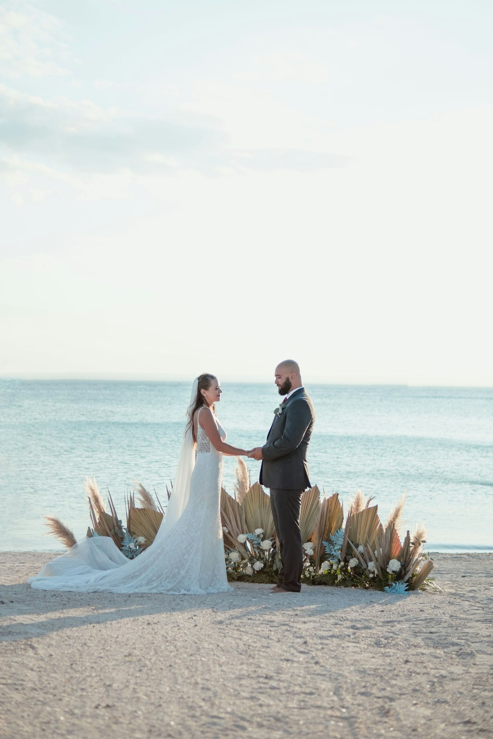 Una sposa e uno sposo in piedi su una spiaggia tenendosi per mano