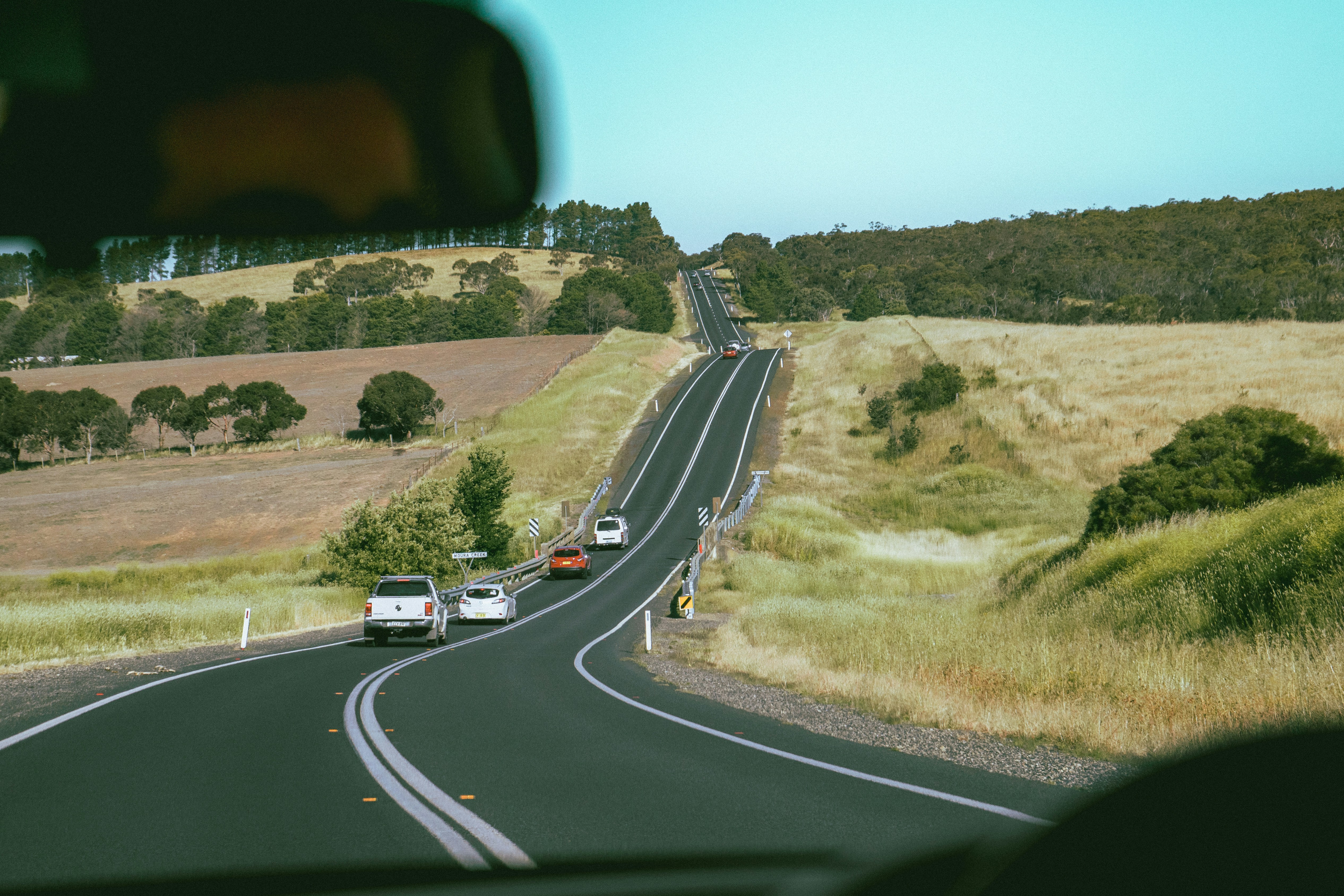 a car driving down a road next to a lush green hillside