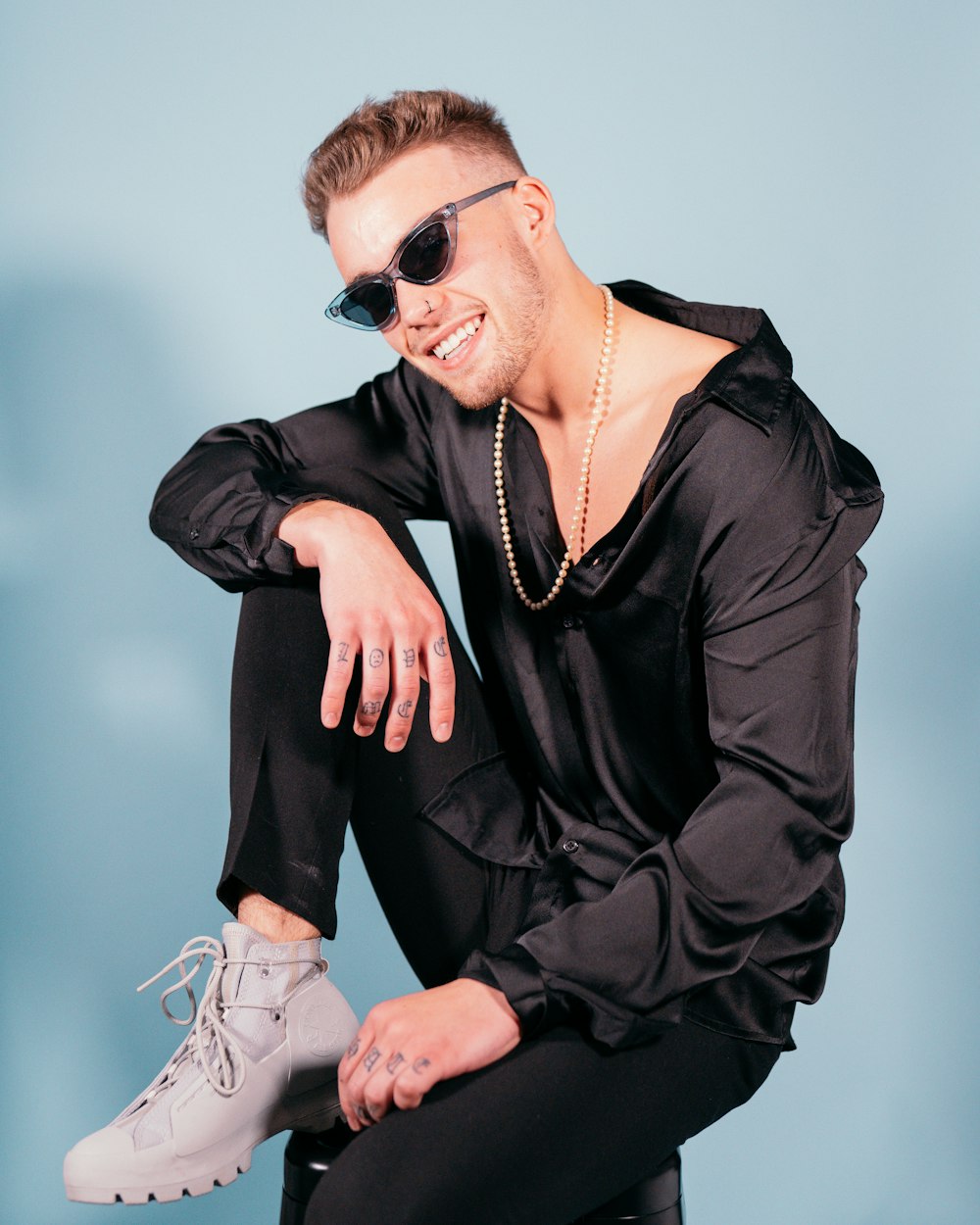 a man in a black shirt and sunglasses sitting on a stool