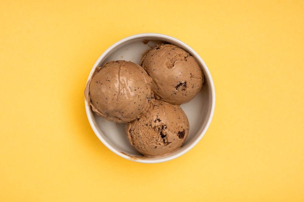 three scoops of ice cream in a bowl on a yellow background
